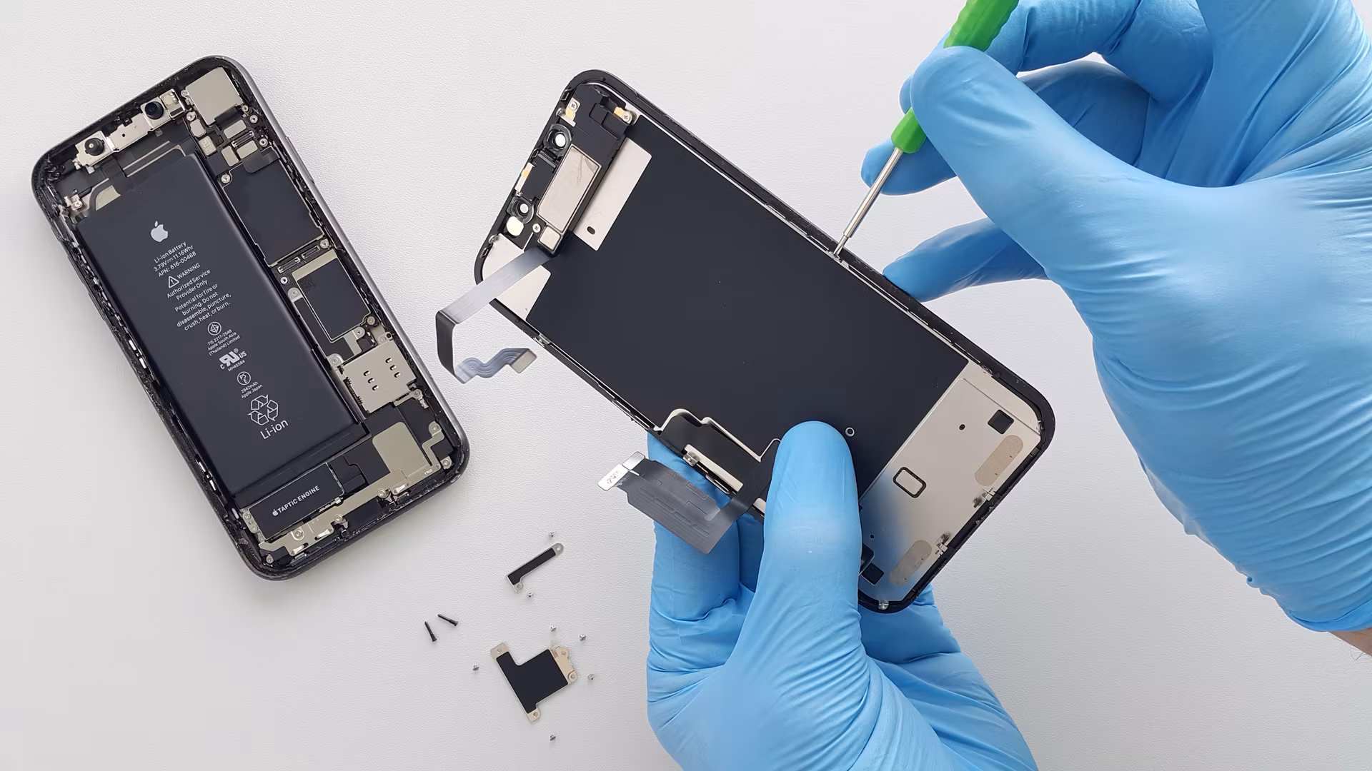 Technician in blue gloves fitting a replacement display to an opened iPhone